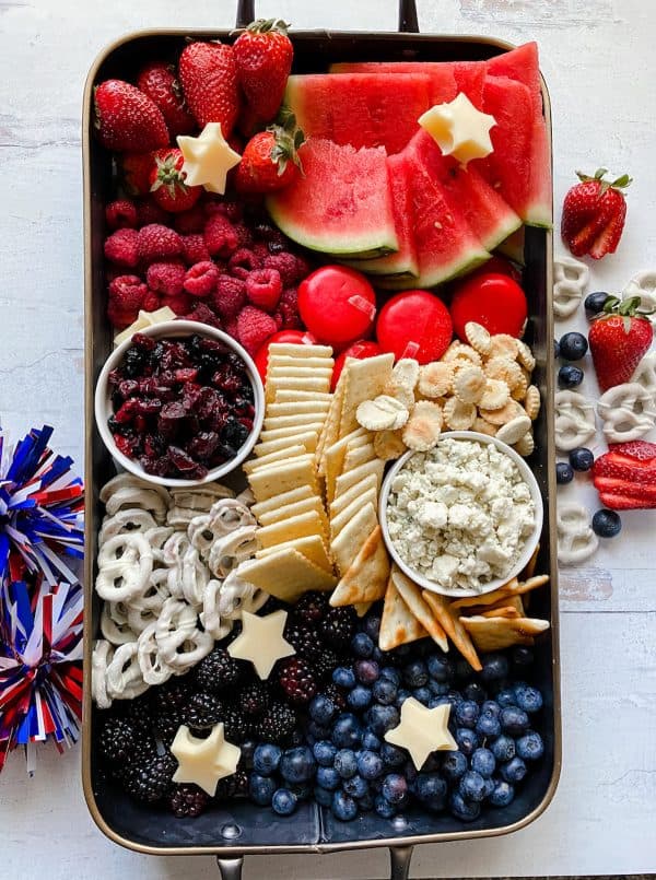 an organized red, white, and blue board with crackers, chocolate covered pretzels, fruit, and more from cheese and such.