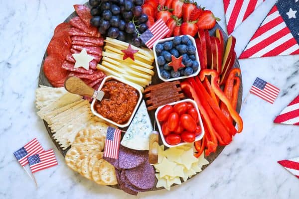 A round board with bowls of salsa, blueberries, and tomatoes, Also including meats, cheese, and crackers from fab everyday. 