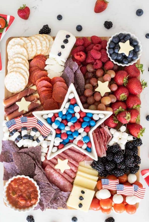 A star shaped bowl of m&ms sits on a board surrounded by meat, cheese, and fruit from Jennifer Maune. 4th of july charcuterie board ideas do not need to be completely red, white, and blue. 