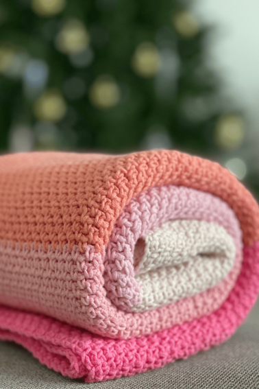 Colorful crochet blanket rolled up in front of a blurred background.