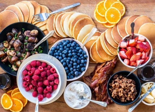 AllRecipes pancake charcuterie board with fruit, a skillet of mushrooms, and more. 