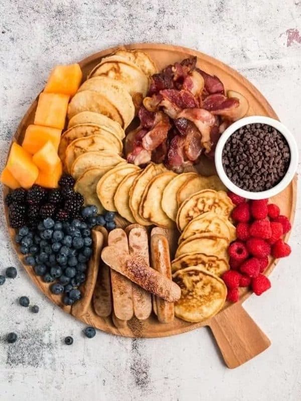 Natural deets has created a charcuterie board with pancakes, fruit, bacon, and sausage. 