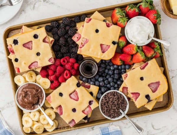 a delicious sheet pan pancake with blueberries, strawberries, and toppings galore from sparkles to sprinkles.