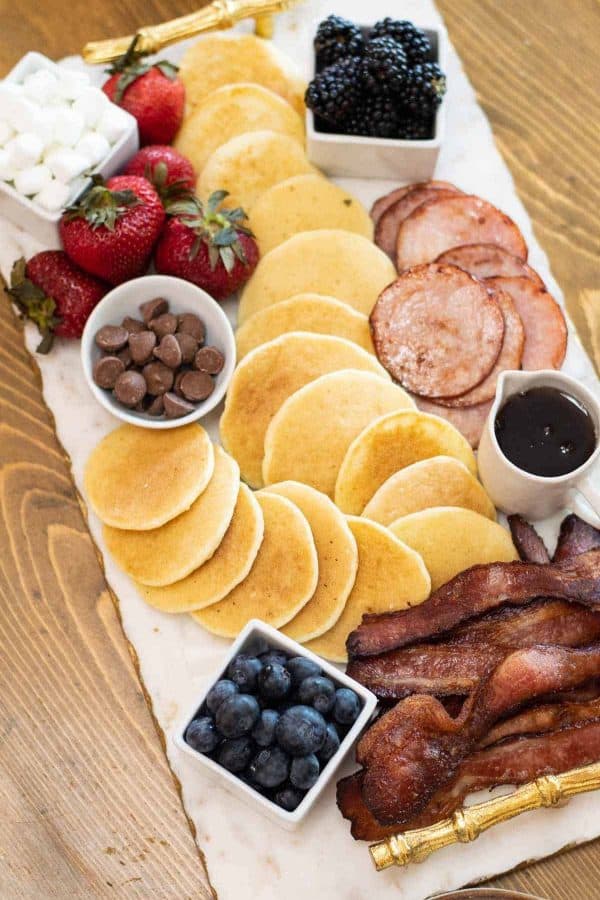 a pancake board with bacon, toppings, and syrup. 