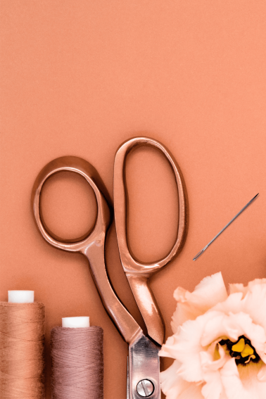 Image shows thread, scissors and other sewing essentials over a brown background.