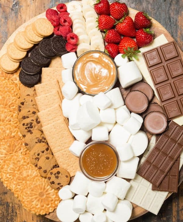 a large board from Cooking with Janica full of berries, cookies, candy, chocolate, dips and marshmallows.