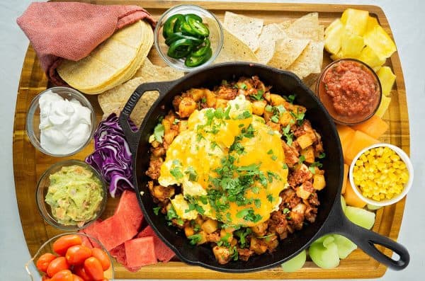 breakfast tacos with a skillet full of potatoes topped with egg and cheese. It's surrounded by watermelon, chips, pineapple and more from Barbara Eats.