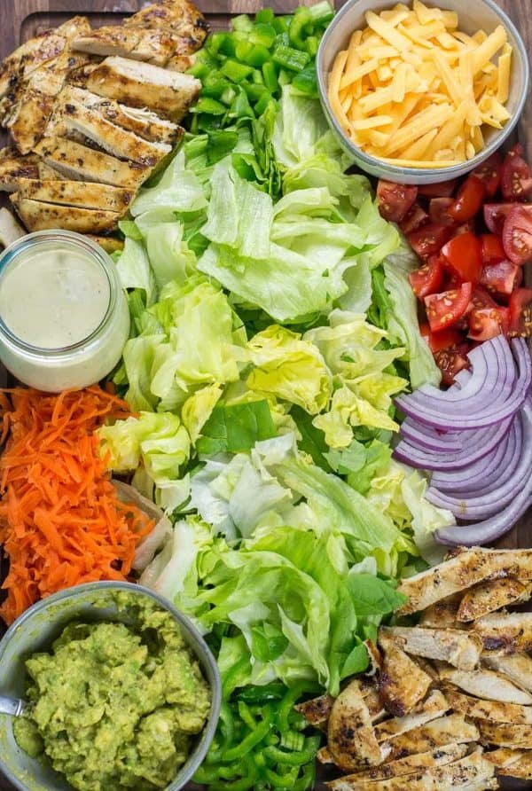 A chicken taco salad board with tomatoes, carrots, onion, guacamole, and other toppings from it starts with good food.