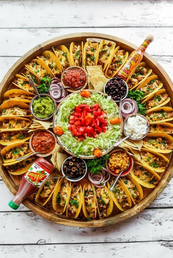 The Reluctant Entertainer's charcuterie board with over 50 mini tacos, and all the fixings in the middle.