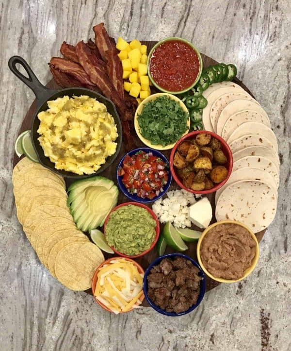 A spin on the taco charcuterie board ideas with breakfast tacos. The Baker mama includes, eggs, bacon. potatoes, and the traditional taco add-ons.
