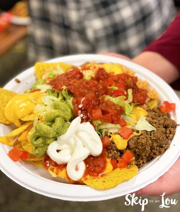 A person holding a plate with nachos with beans, guacamole, cream, and beef.
