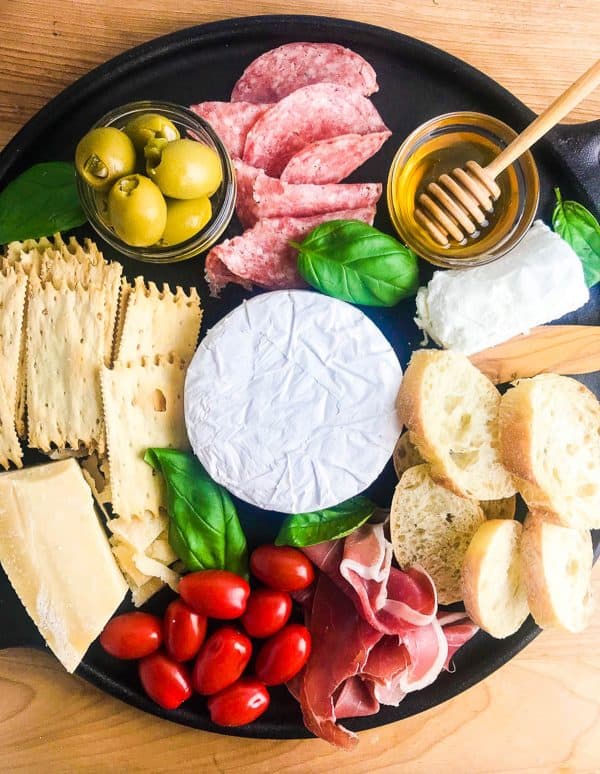 a round board with bread, crackers, tomatoes, and meat from life ambrosia.