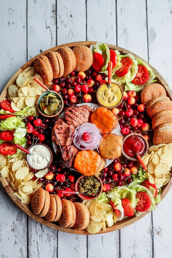 a round board with the fixings for hamburgers including the condiments, buns, and veggies from reluctant entertainer.