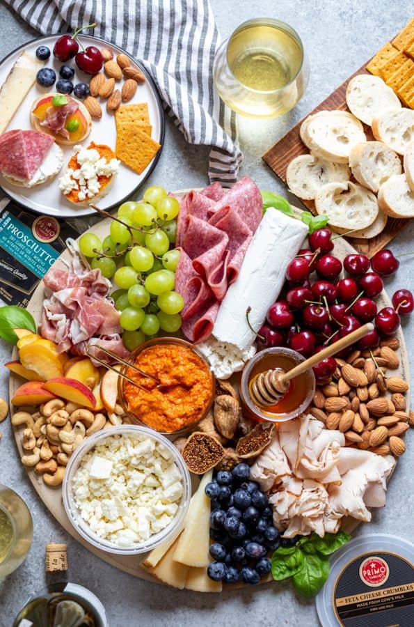 a round board from strawberry blodie kitchen with cheese, dips, meat, and fruit.