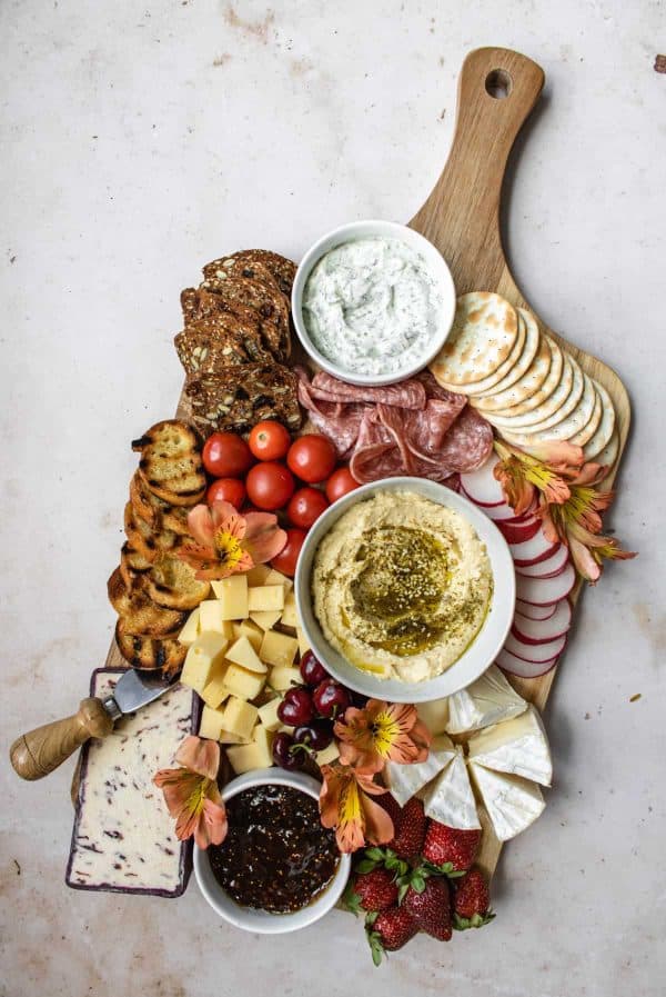 a charcuterie board with hummus, crackers, veggies, and a variety of cheeses from the powdered apron.