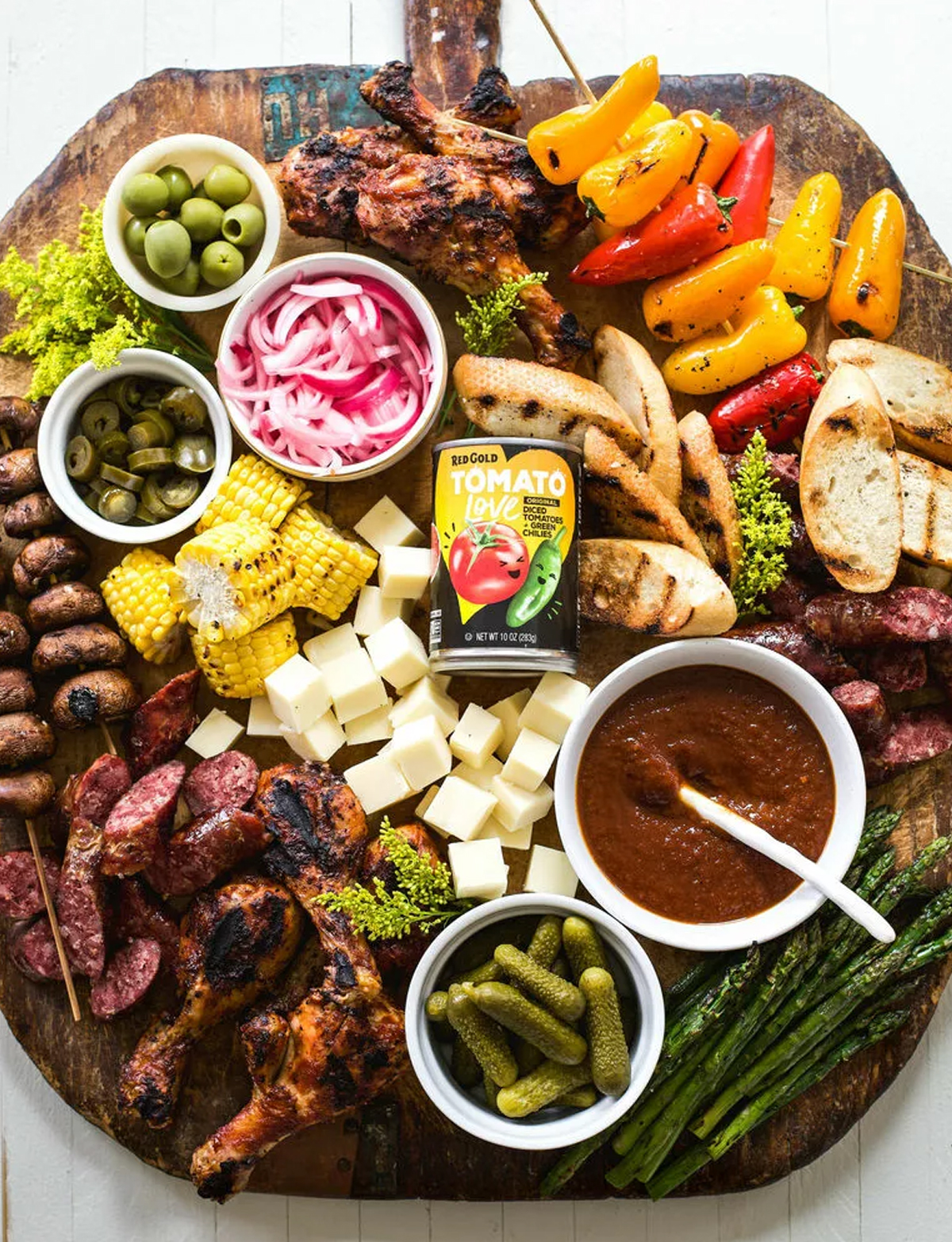 A large board with a variety of choices including chicken drumsticks, bella mushrooms, and grilled veggies from the feedfeed.