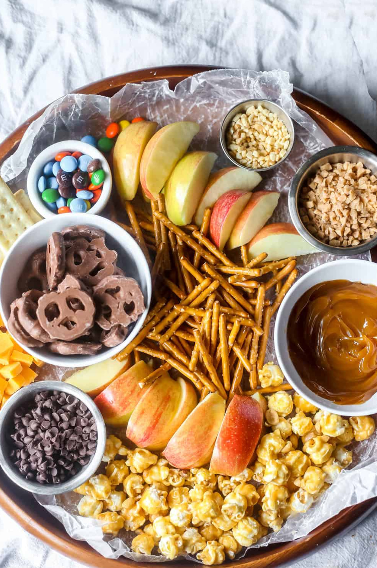 B sugar mama's caramel apple board showcases m&m;s, nuts, chocolate chips, caramel sauce, apples, and caramel popcorn.