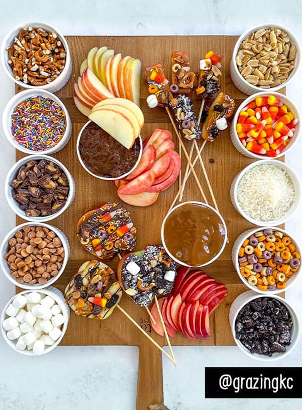 Sprouts Caramel Apple Charcuterie Board presents sliced apples, caramel topping, sprinkles, candy corn, nuts, pretzels, Oreos, and marshmallows.