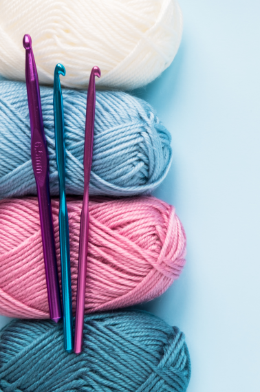Image shows three different crochet hooks in purple and blue and four different skeins of yarn.