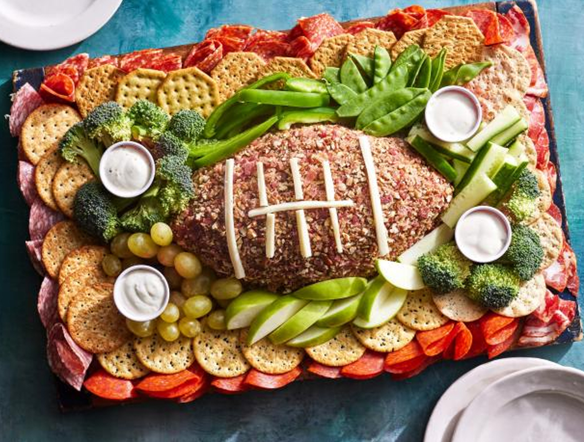 Food Network Kitchen's football charcuterie board displays a football cheese ball, deli meats, cheese, and veggies.