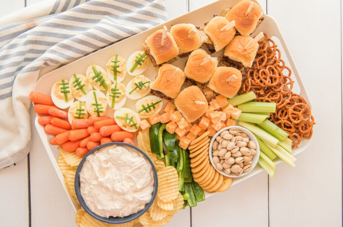 Football shaped deviled eggs, mini sliders, veggies, chips, and dips fill Kitchen Divas football board.