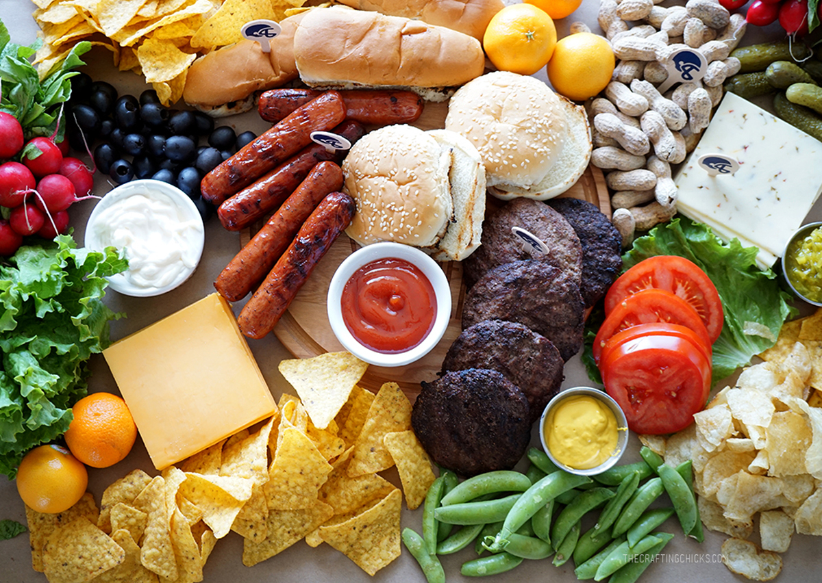 Hot dogs, hamburgers, cheese, chips, and fruit are showcased on The Crafting Chicks Super Bowel Sunday board.