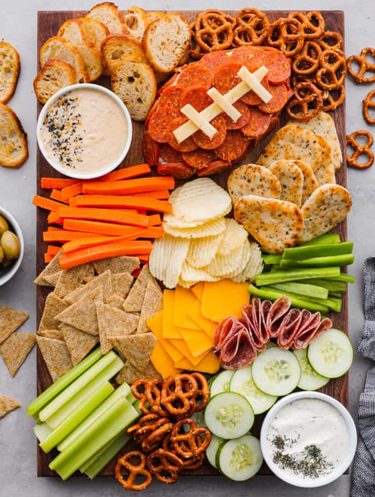 Pepperoni football, bell peppers, cucumbers, crackers, chips, pretzels and dip fill The Recipe Critic's football board.