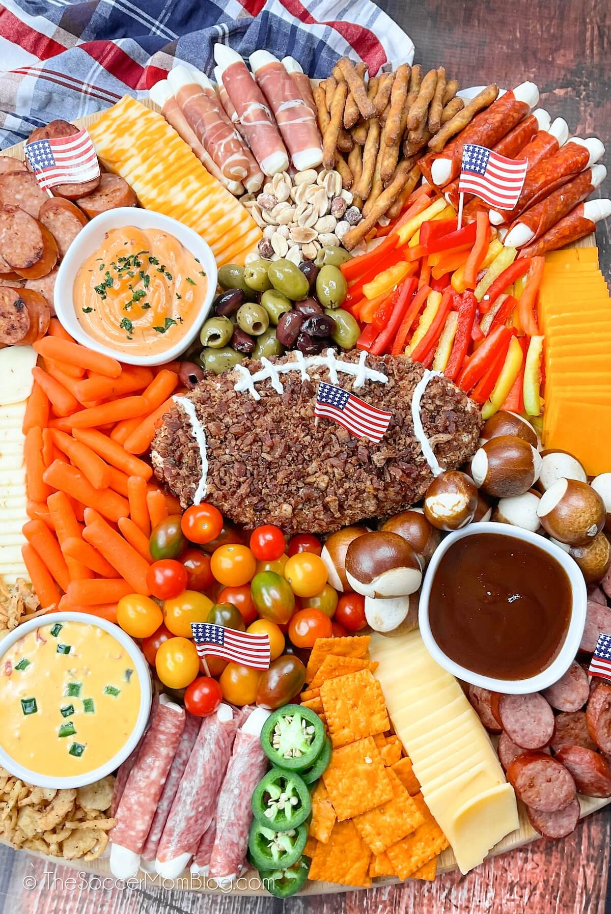 Bacon wrapped cheese football, cheese crackers, tomatoes, carrots, olives, pretzels, and nuts fill Soccer Mom Blog's charcuterie board.