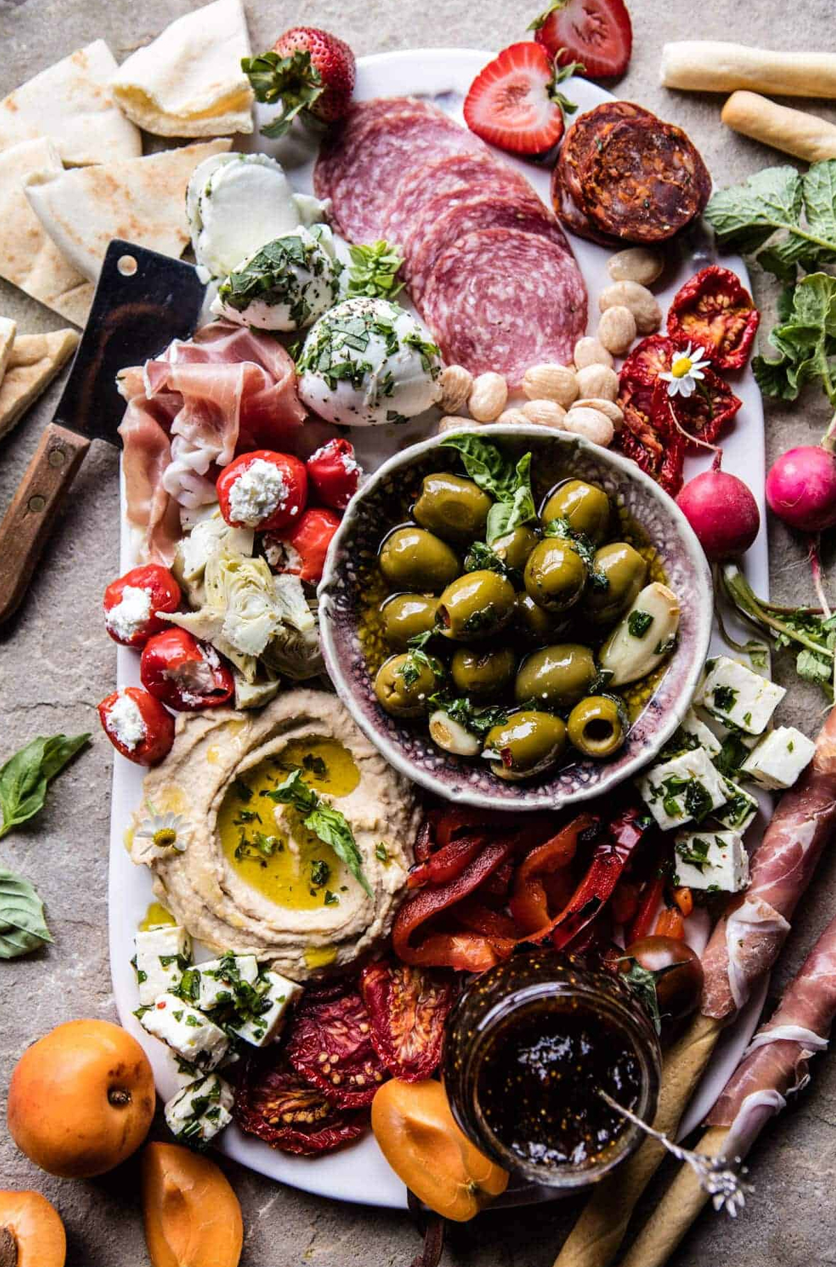 a more traditional charcuterie board with some greek twists from half baked harvest with charcuterie meats. cheese, and some stuffed peppers and hummus.