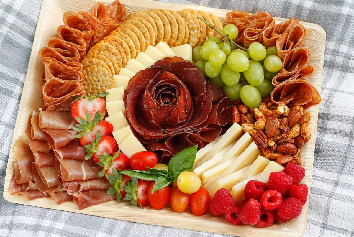 a charcuterie board from volpi foods with a salami rose in the middle with crackers, cheese, and fruit