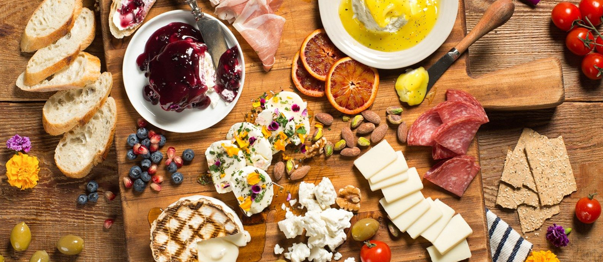 a wooden board with cheese, fruit, spreadable cheese covered in sauces, and bread from woolwich dairy.
