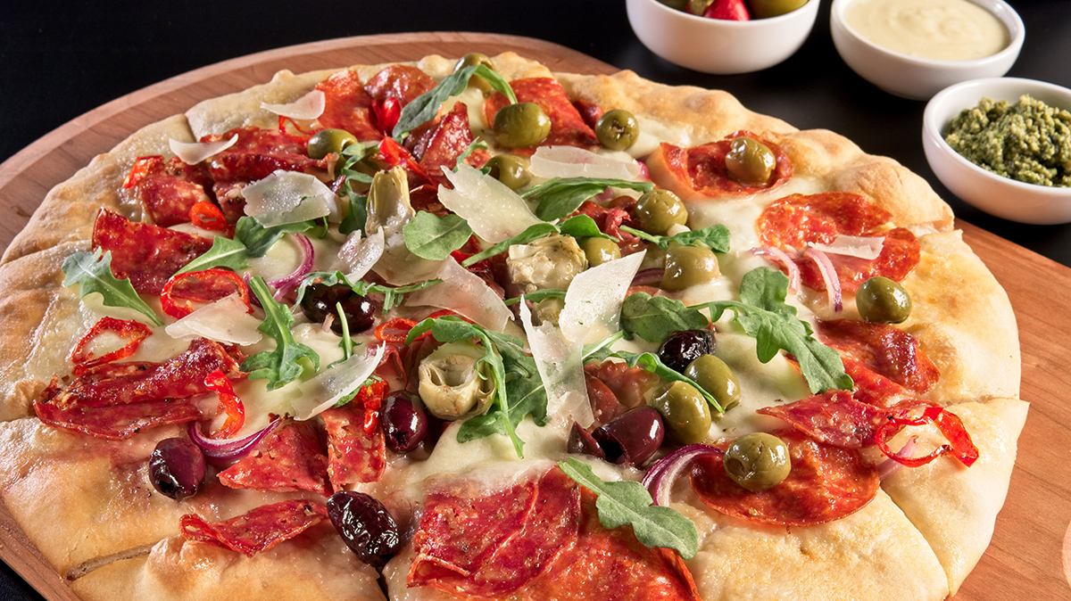 Grande Cheese charcuterie board pizza shows a pizza filled with pepperoni, olives, cheese, and red onions.