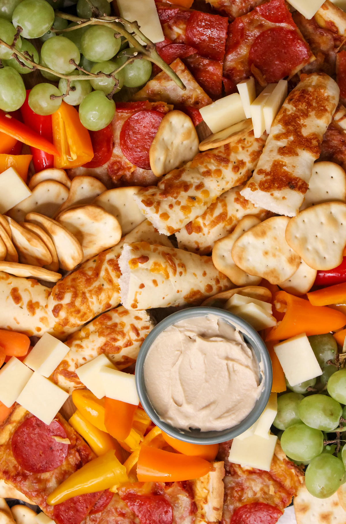 Mozielife's pizza board shows breadsticks, sliced pepperoni and cheese pizza, veggies, and grapes.