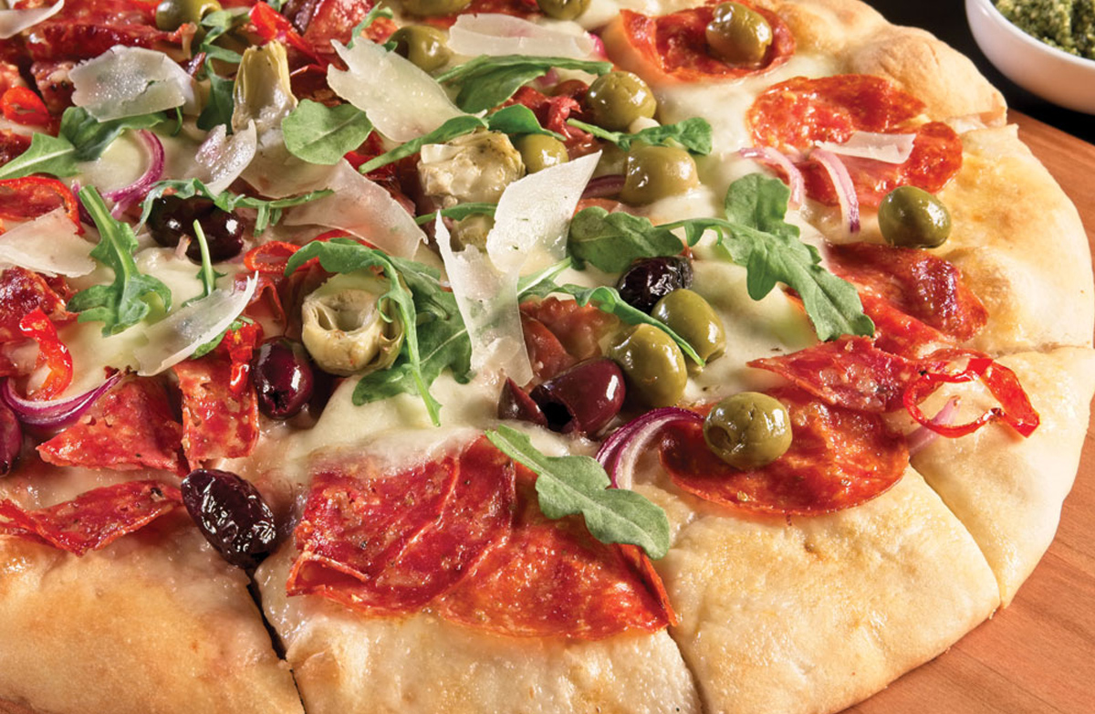 PMQ Pizza Magazine's pizza charcuterie board is full of a pizza with pesto sauce, peppadew slices, and marinated artichoke hearts, 