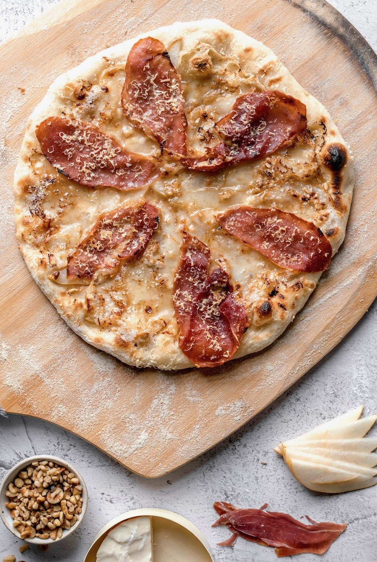 The Practical Kitchen board displays a delicious pizza topped with thinly sliced pears, chopped walnuts, and brie,