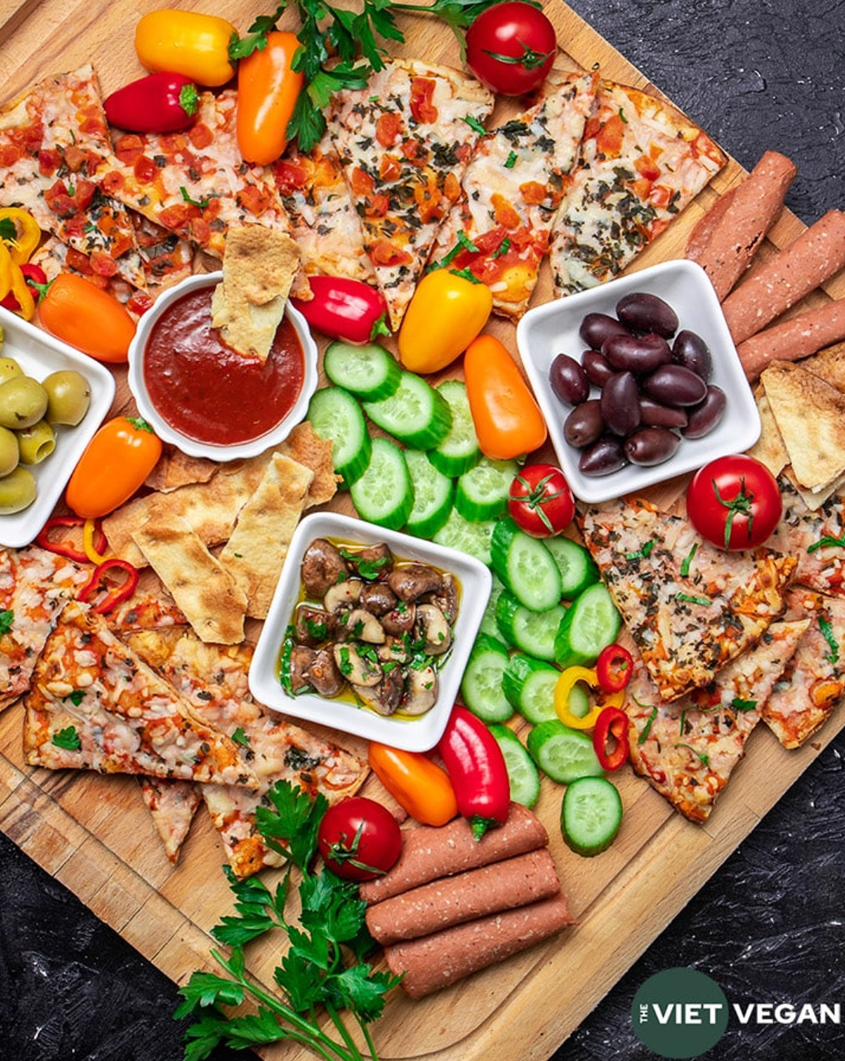 The Viet Vegan's showcases a vegan pizza board with mushrooms, olives, tomatoes, cucumbers, and a veggie pizza.