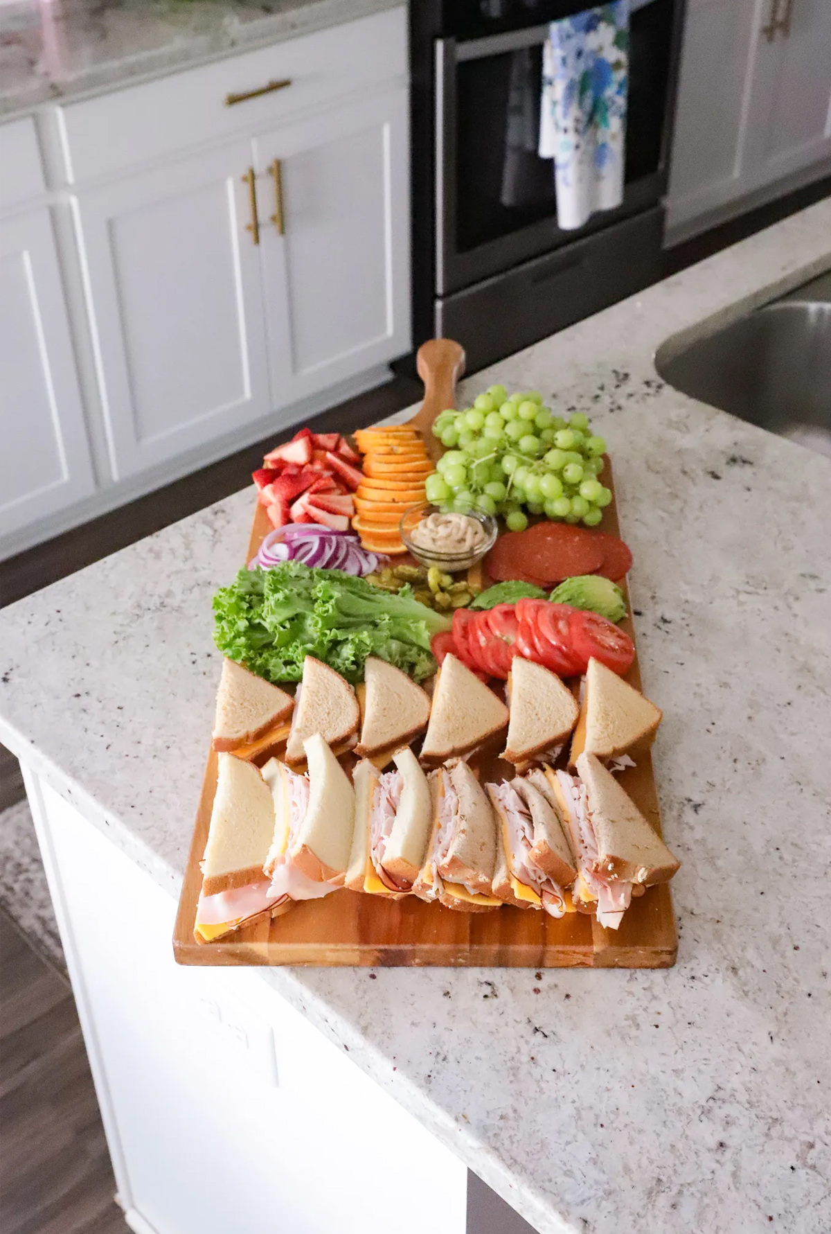 Mattie James sandwich board is full of pre-made sandwiches, veggies, grapes, oranges, and strawberries.