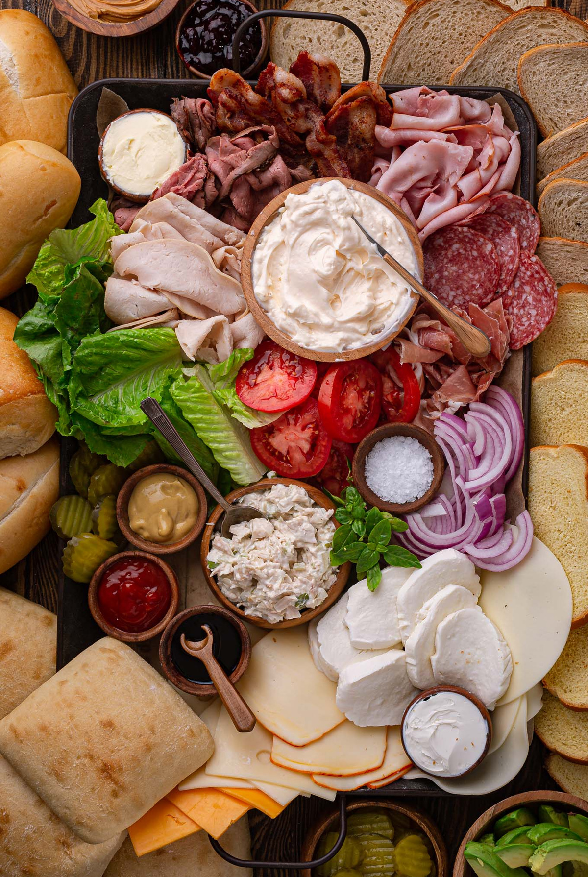 Olivia's Cuisine sandwich charcuterie board is full of meats, cheese, mayo, bacon, lettuce, and bread.