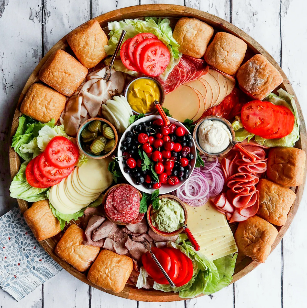 Reluctant Entertainers sandwich board includes rolls, tomatoes, lettuce, meats, onions, pickles, and cheese.