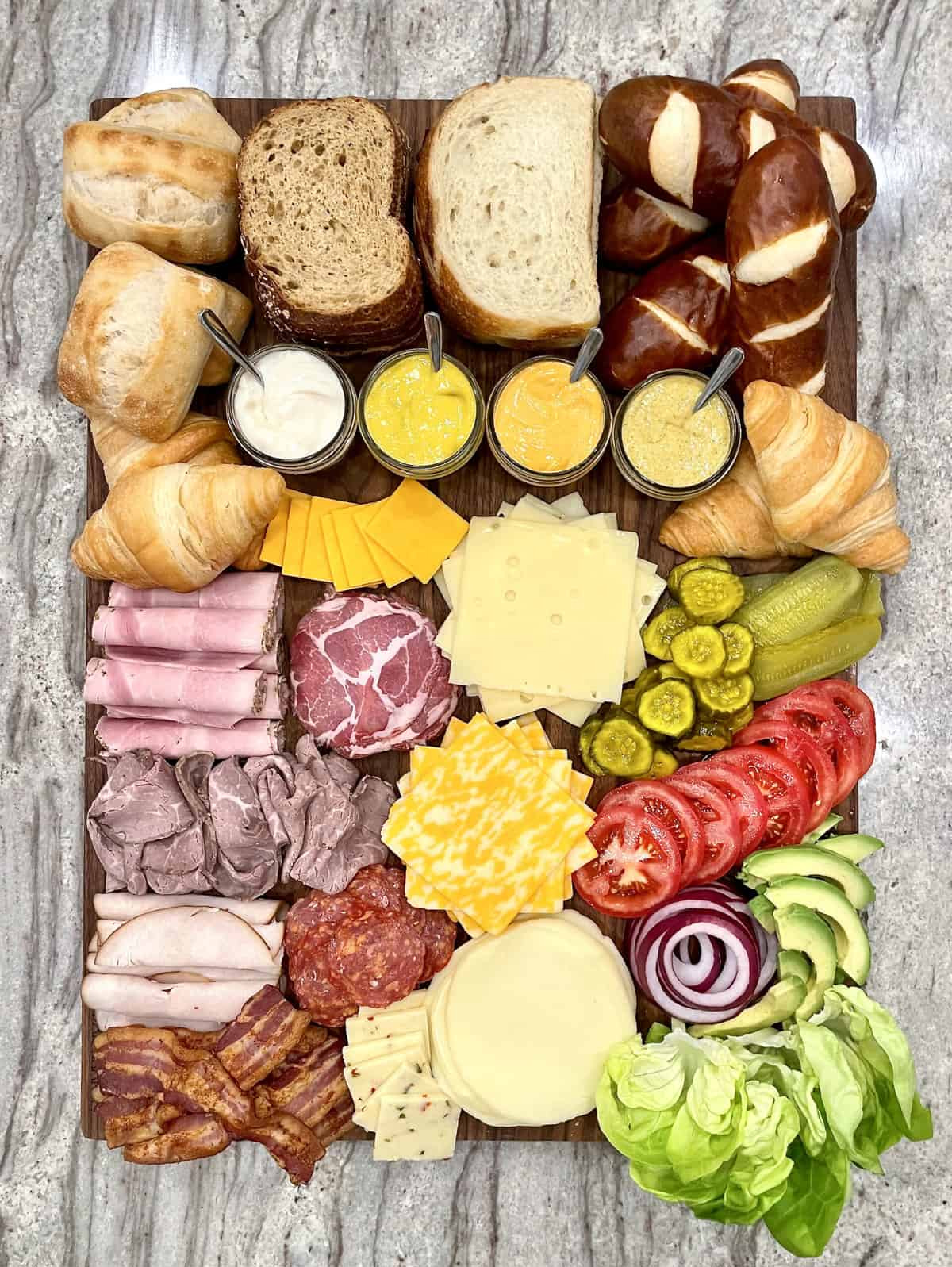 The Baker Mama created a sandwich board full of bread, rolls, deli meats, cheese, dressing, tomatoes, and avocados.