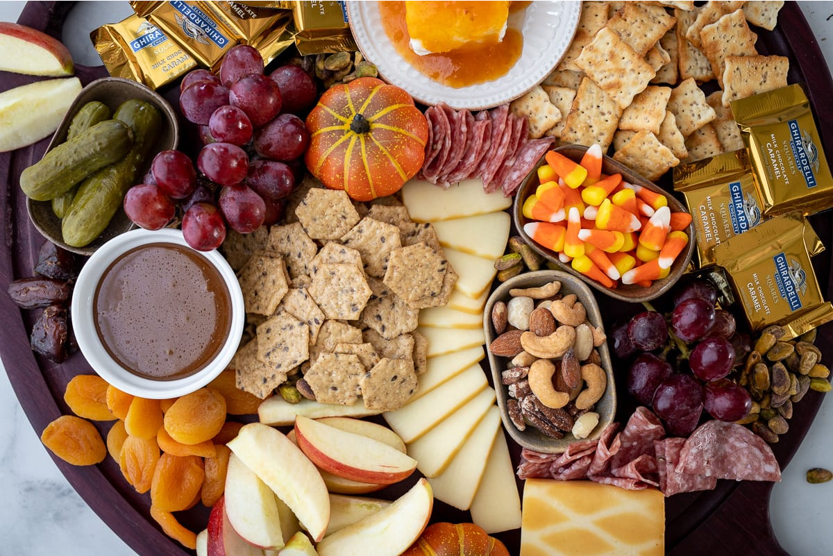 Caramel dip, apple slices, caramel corn, grapes, crackers, meat, cheese, and chocolate fill A Red's Patula's fall charcuterie board