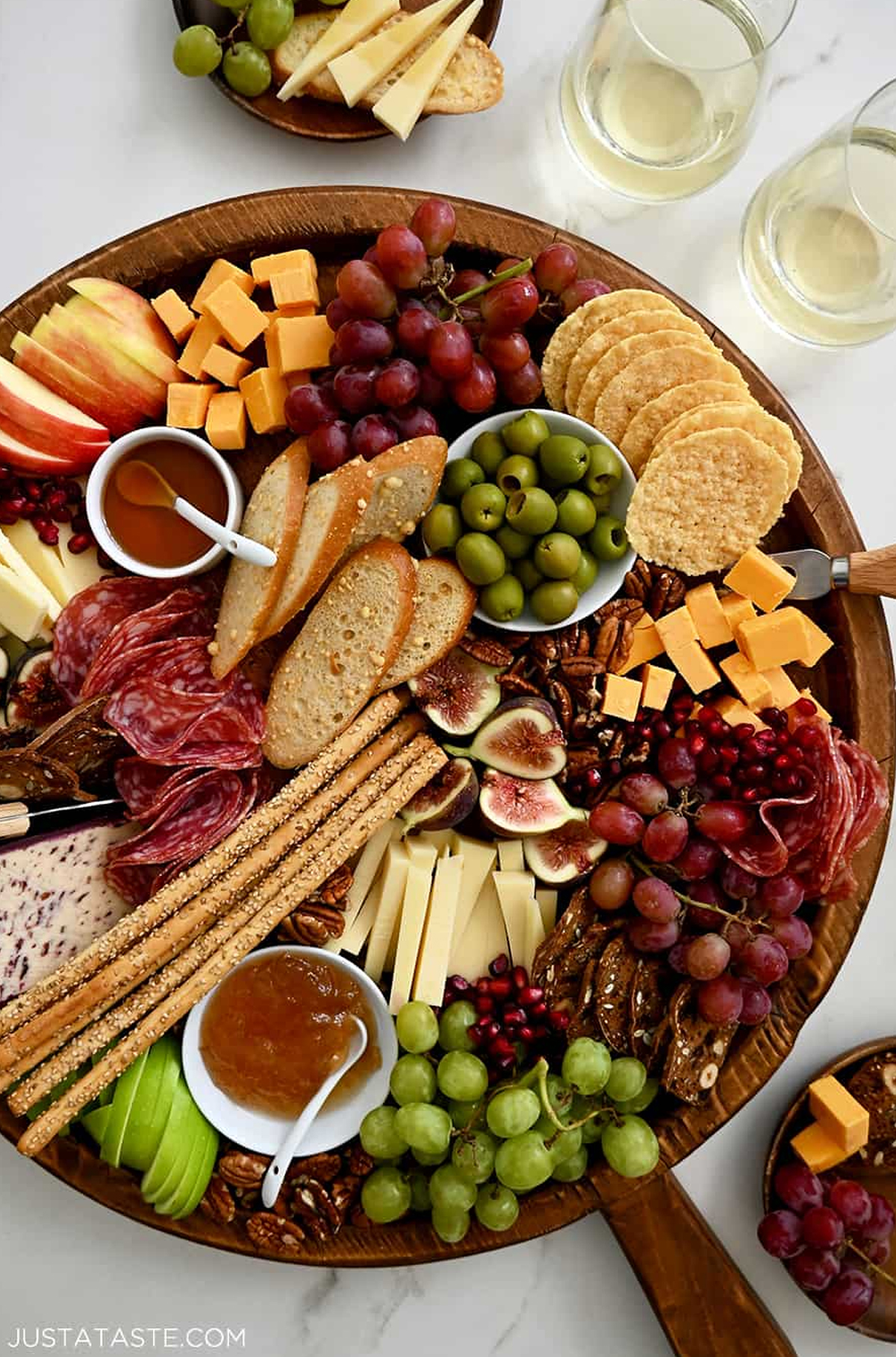 Just a Taste's charcuterie board displays figs, grapes, pomegranate seeds, salami, figs, and pretzel sticks.
