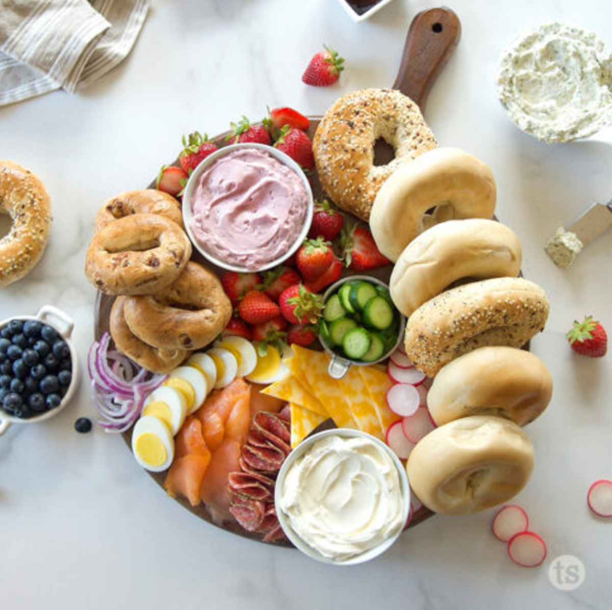 a board with sweet cream cheese options, sliced cheese, radishes, eggs, bagels, and even strawberries from tastefully simple blog.