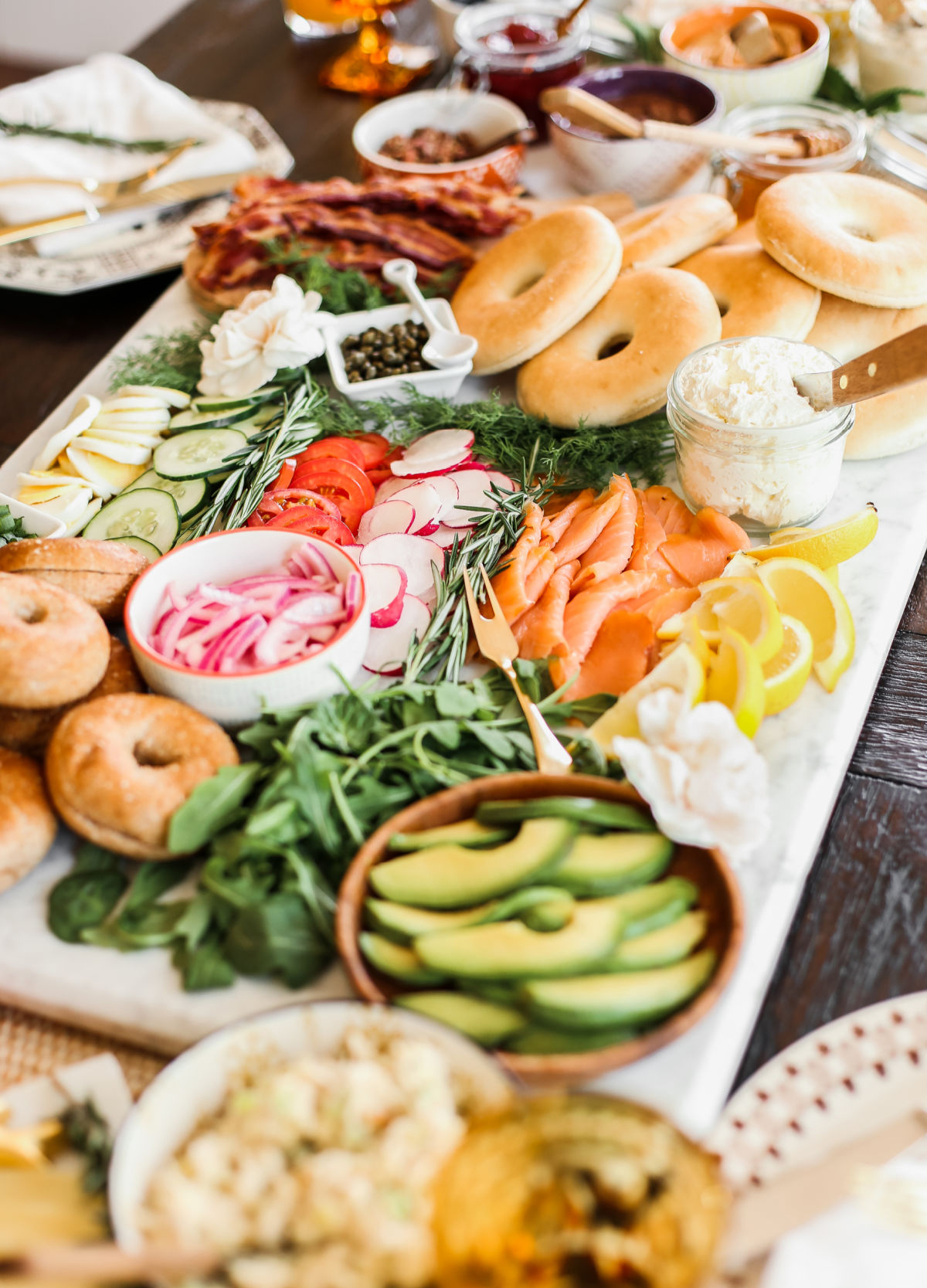 a large board with lemons, greens, bagels, cream cheese, and veggies from celebrations at home.