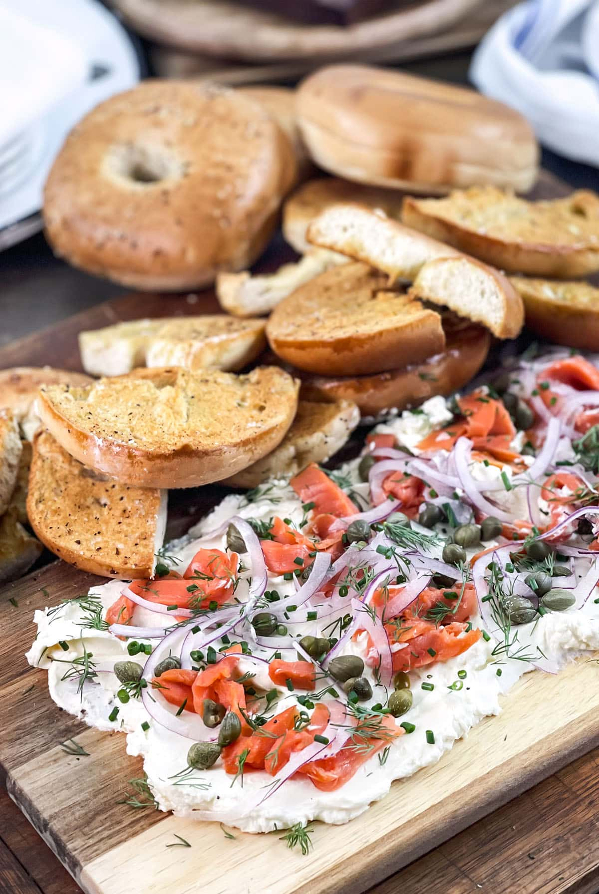 cream cheese spread on a cutting board with capers, red onions, and toasted garlic bagels from cook the story.