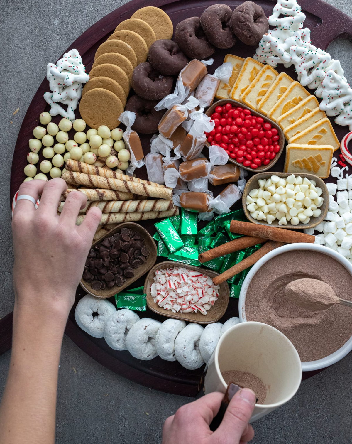 A red spatula creates a cocoa charcuterie board with small bowls of toppings like white chocolate chips, red hots, and more. 