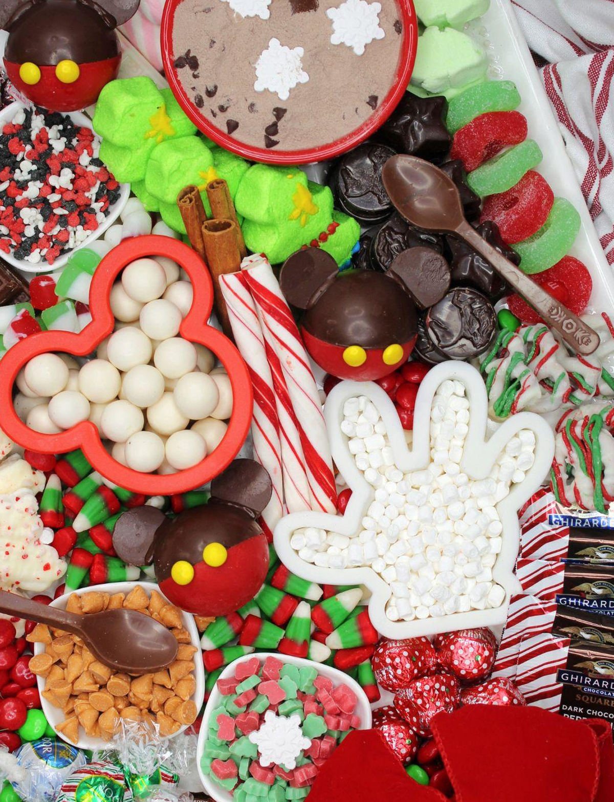 a mickey themed charcuterie board with chocolate spoons, mickey hot cocoa bombs, and plenty of candies from sweet and savory morsels.