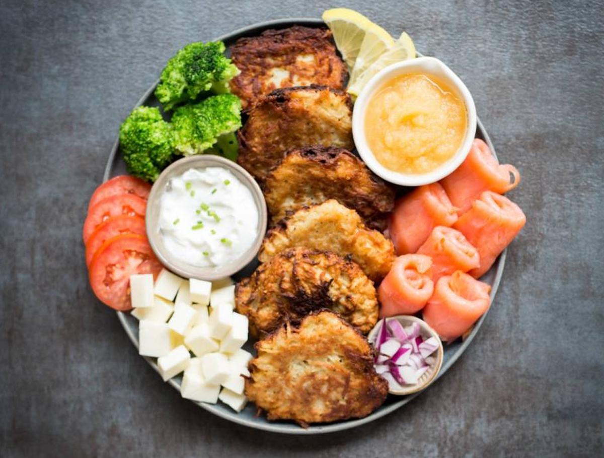 a simple Hanukkah charcuterie board recipe with apple sauce, sour cream, latkes, salmon, and veggies from kosher.com