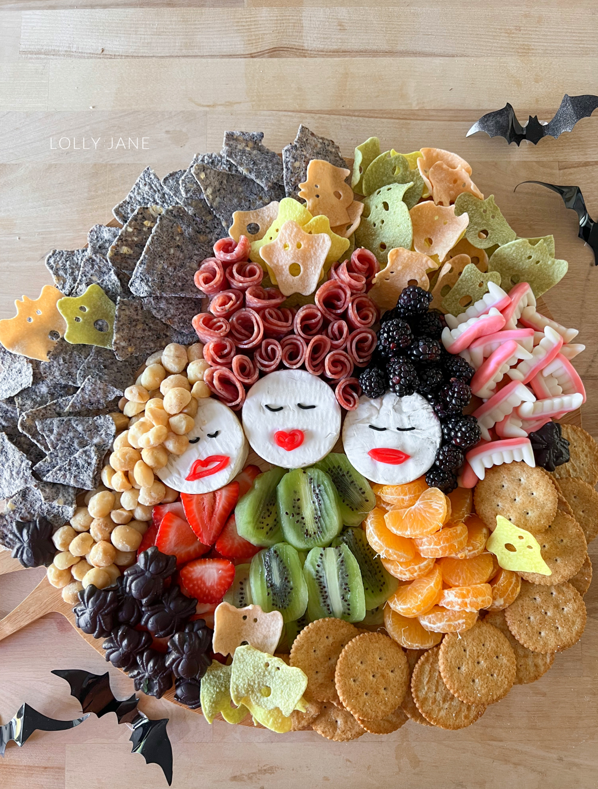 Lolly Jane's charcuterie board displays meats, chips, cheese, crackers, kiwi, berries, and clementine's.