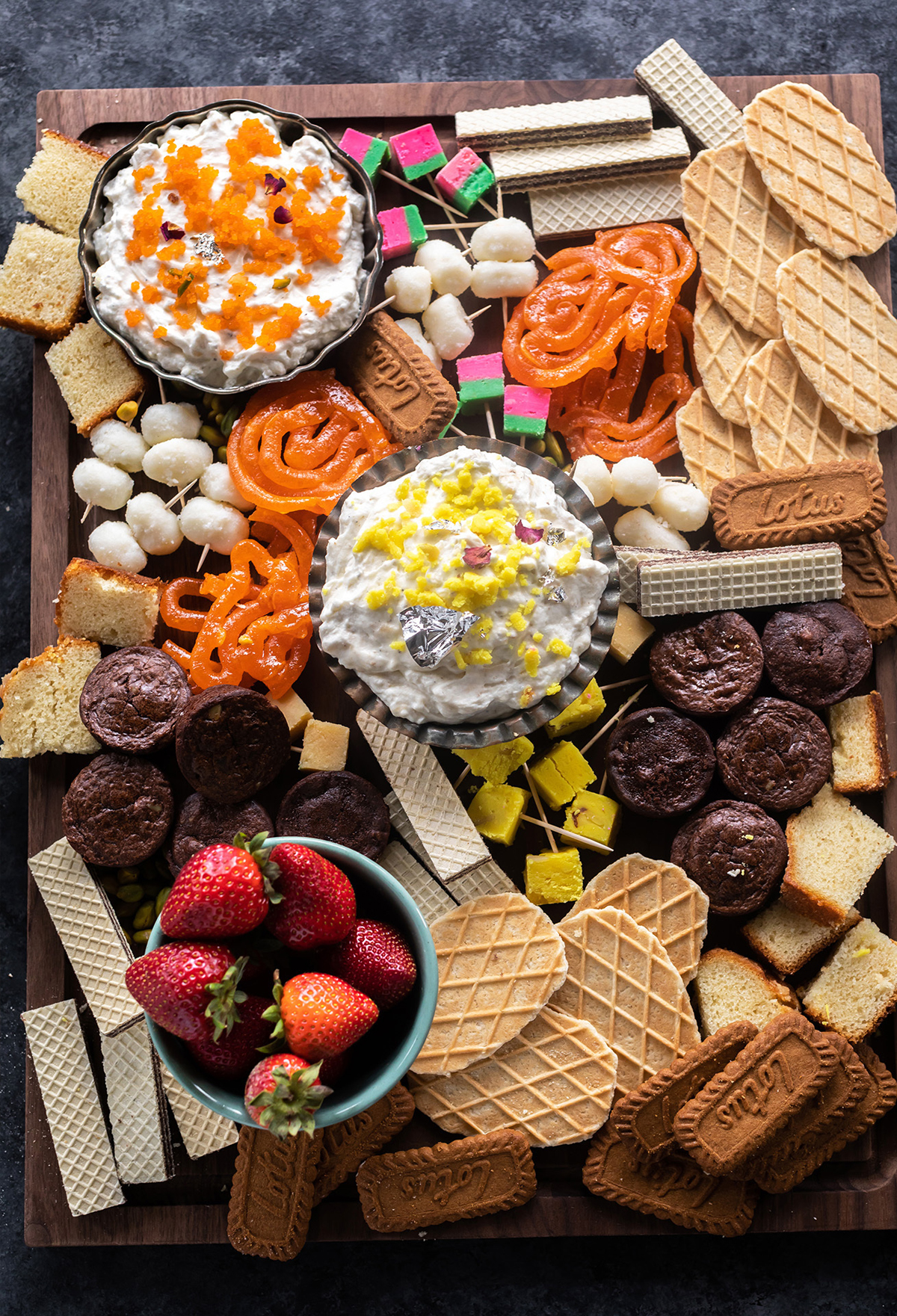 Cook with Manali's dessert board features biscoff cookies, brownie bites, rose burfi, saffron burfi, and pistachio burfi.